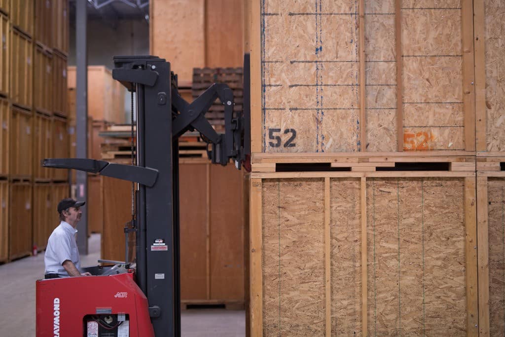 T-R employee wearing a baseball cap and moving storage crates using a red fork lift