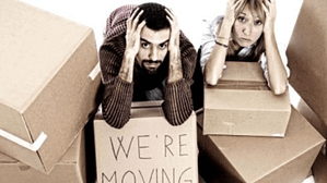 Distressed couple kneeled down surrounded by moving boxes with their hands to their heads