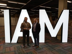 Two men in front of a white IAM conference logo representing Tippet-Richardson