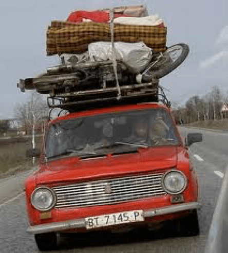 Man, in an old red car, trying to move his personal belongings that is tied on the roof of his car