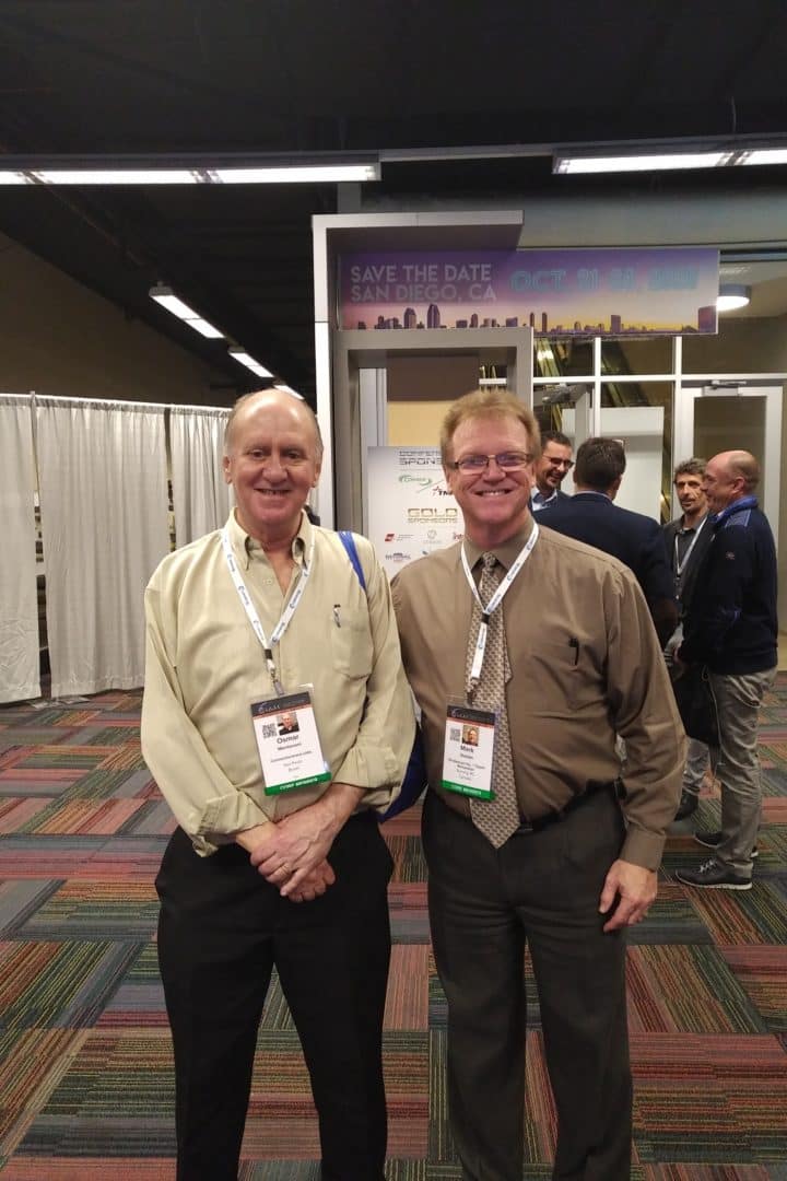 Two middle aged men at a conference in front of a booth
