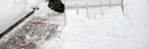 Man, wearing a brown pair of pants and black shoes is shoveling snow off his pathway to his front door